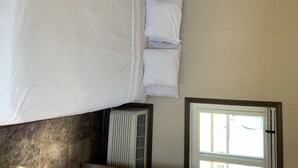 Un lit avec une literie blanche, dans une pièce dont le sol est carrelé et qui possède une fenêtre avec des rideaux.