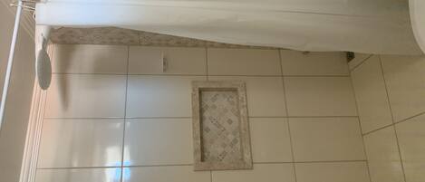 A bathroom with white tiles, a shower curtain, and a small framed picture on the wall.
