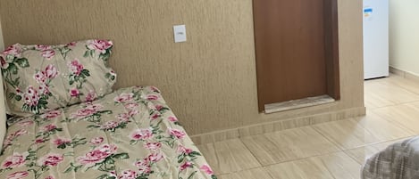 Un dormitorio con cama, televisión instalada en la pared, una puerta y una ventana.