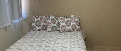 A bedroom with a patterned bedspread, matching pillows, and a wooden floor.