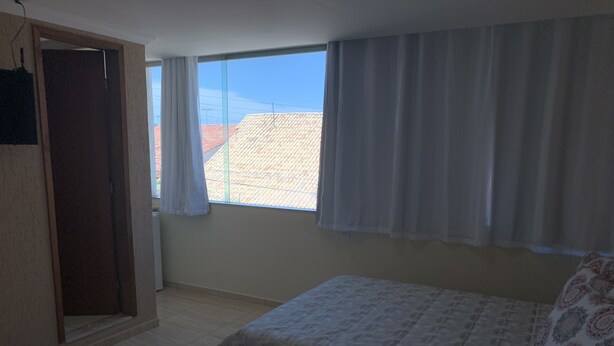 A bedroom with a bed, a window with curtains, a door, and a tiled floor.