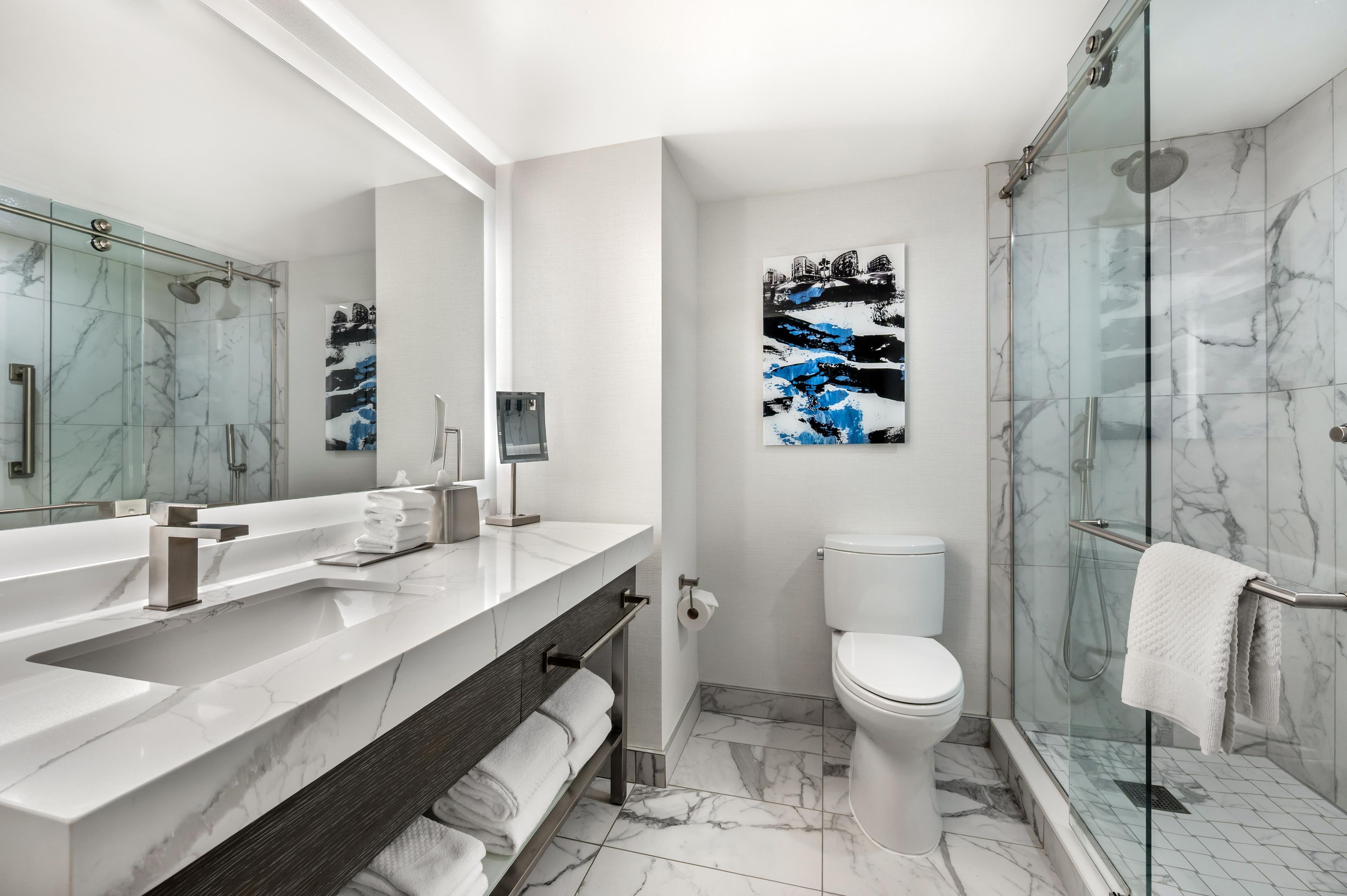 A modern bathroom with a glass shower enclosure, a white toilet, and a marble-tiled floor.