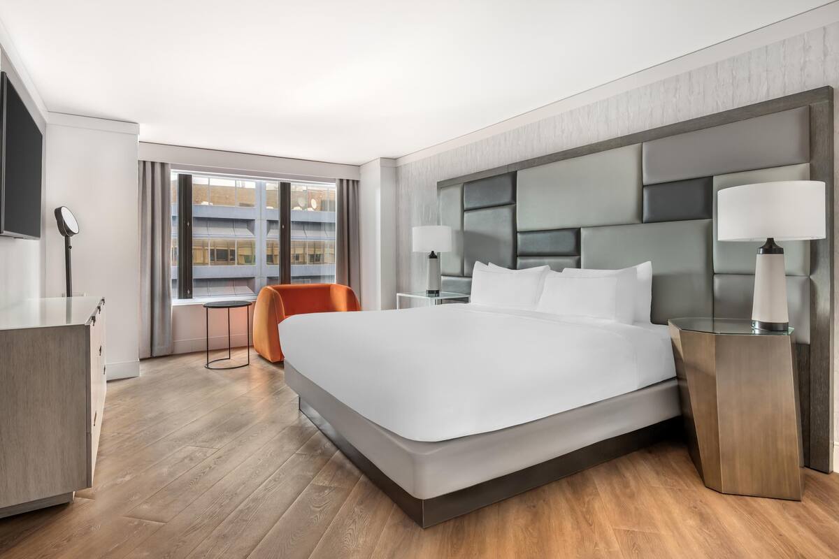 Una habitación de hotel moderna con una cama grande, un escritorio, una silla y vistas a la ciudad.