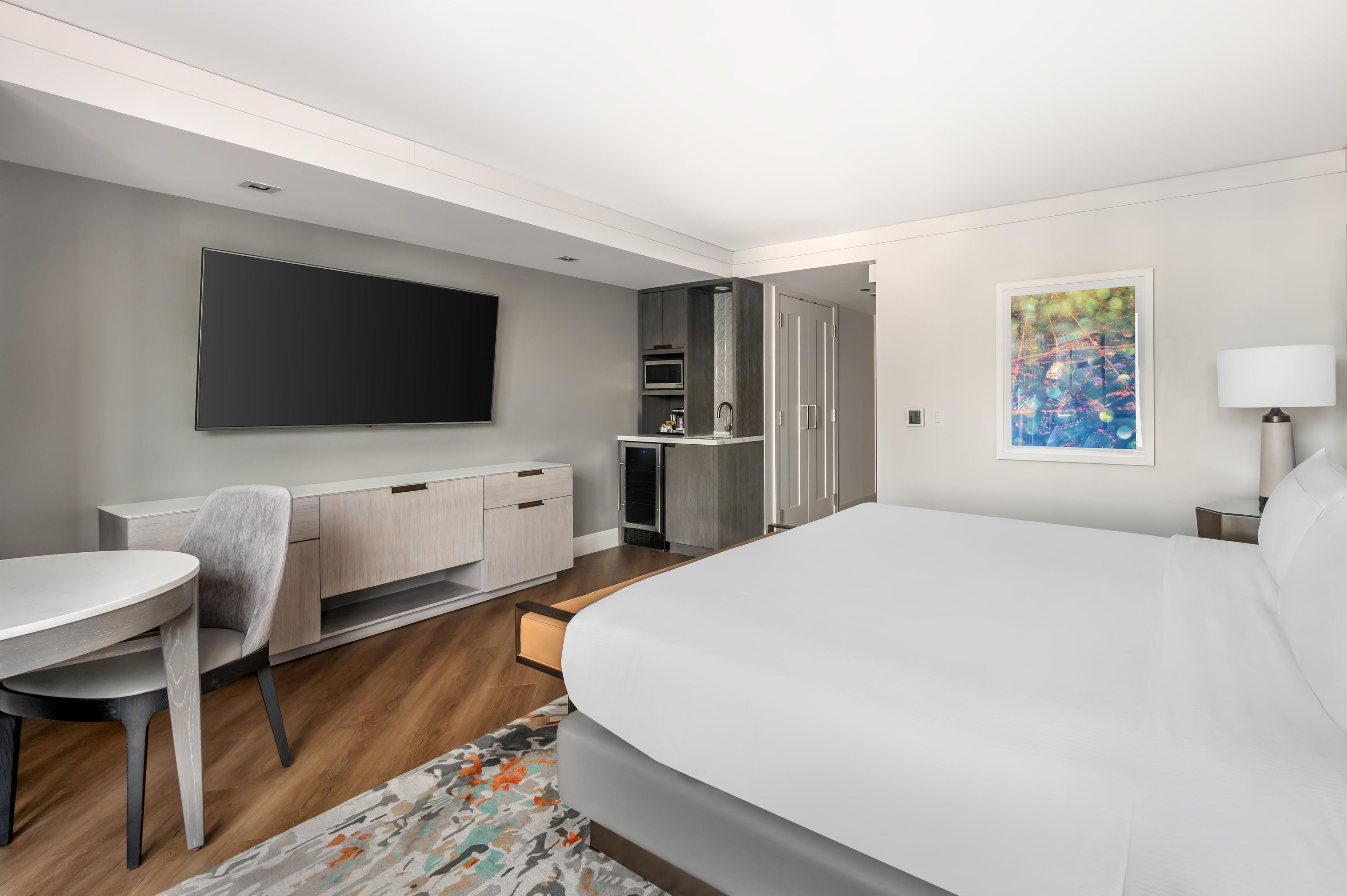 A modern hotel room with a bed, a desk, a chair, a television, a wardrobe, and a bathroom.