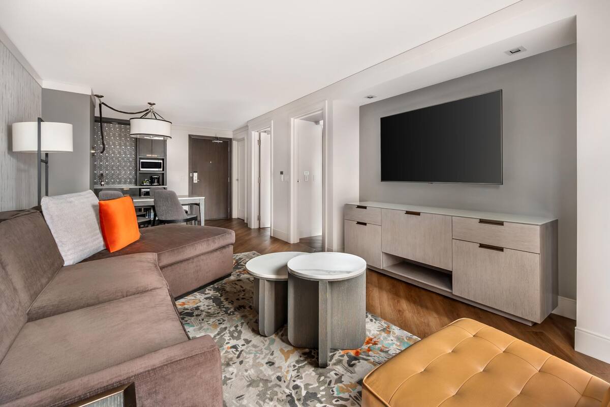 Una sala de estar moderna con un sofá, un reposapiés, una mesa de centro redonda y un televisor fijado a la pared.