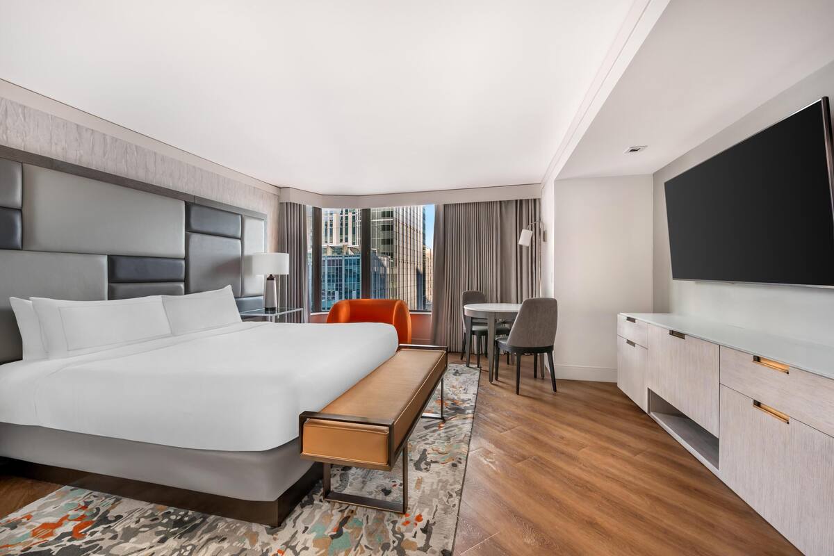 Una habitación de hotel moderna con una cama grande, un escritorio, una silla, un televisor y vistas a edificios.