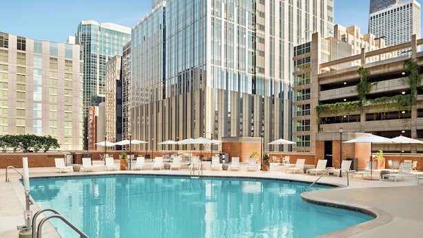 Una piscina con sillones de descanso y sombrillas, rodeada de edificios altos.