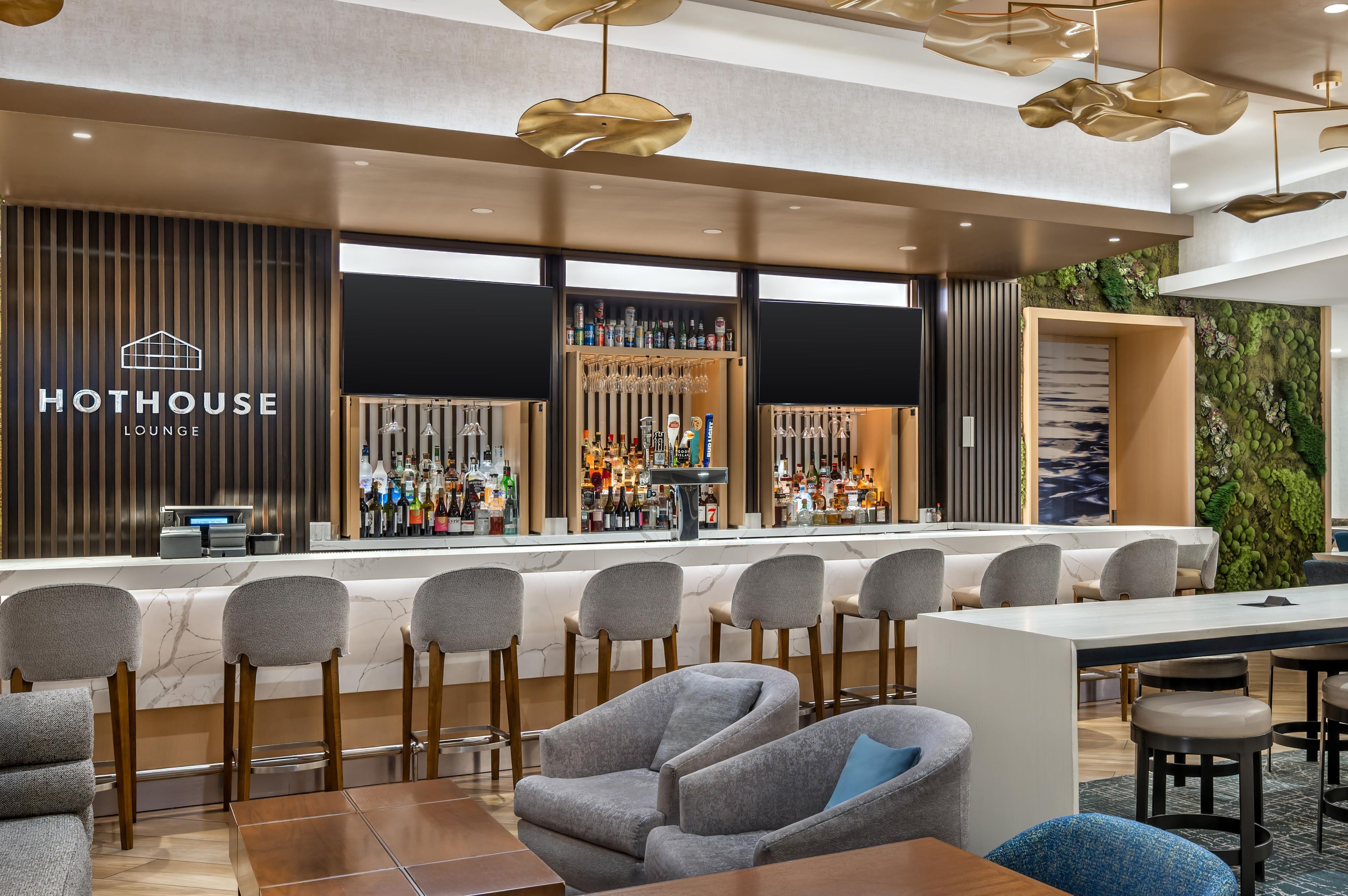 Un moderno espacio de lounge con barra, asientos y un letrero que dice 'HOTHOUSE LOUNGE'.