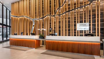A modern hotel reception with a wooden panel wall, marble reception desk, and a sign indicating member & guest check-in.