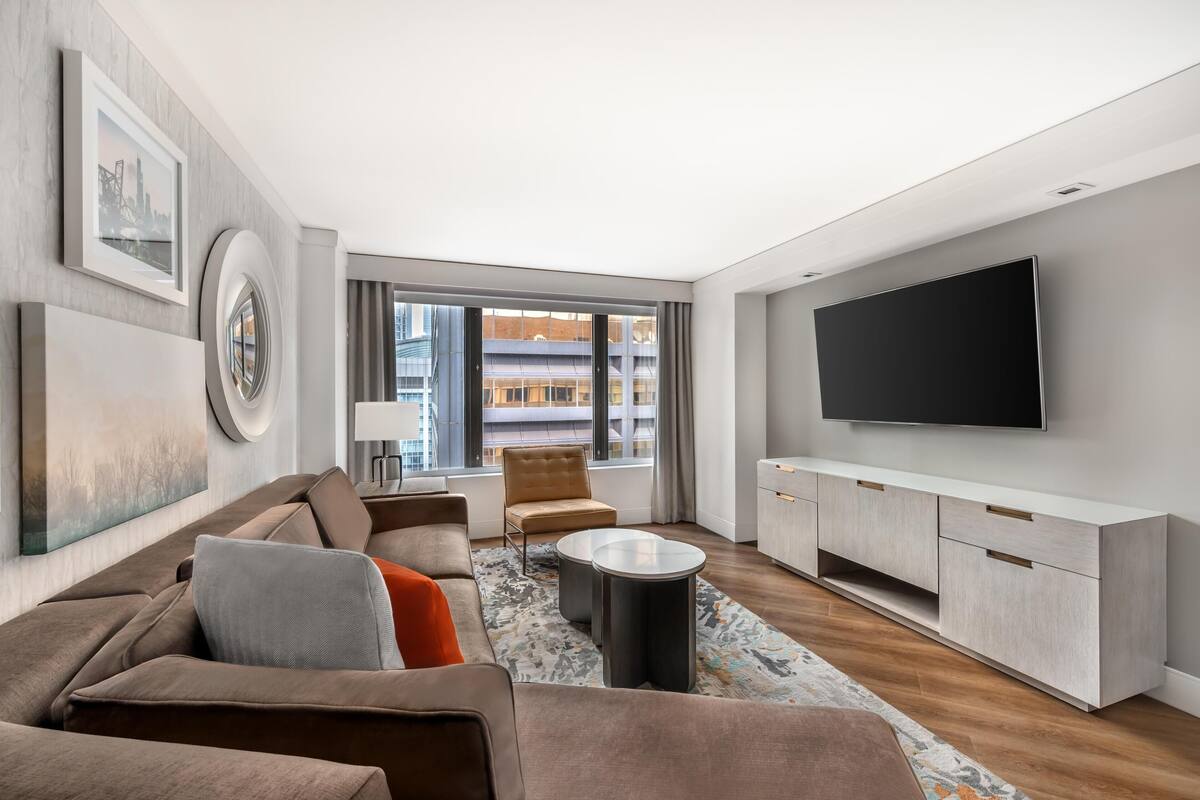 Una sala de estar moderna con sofá, mesa de centro, televisor y vista a la ciudad.
