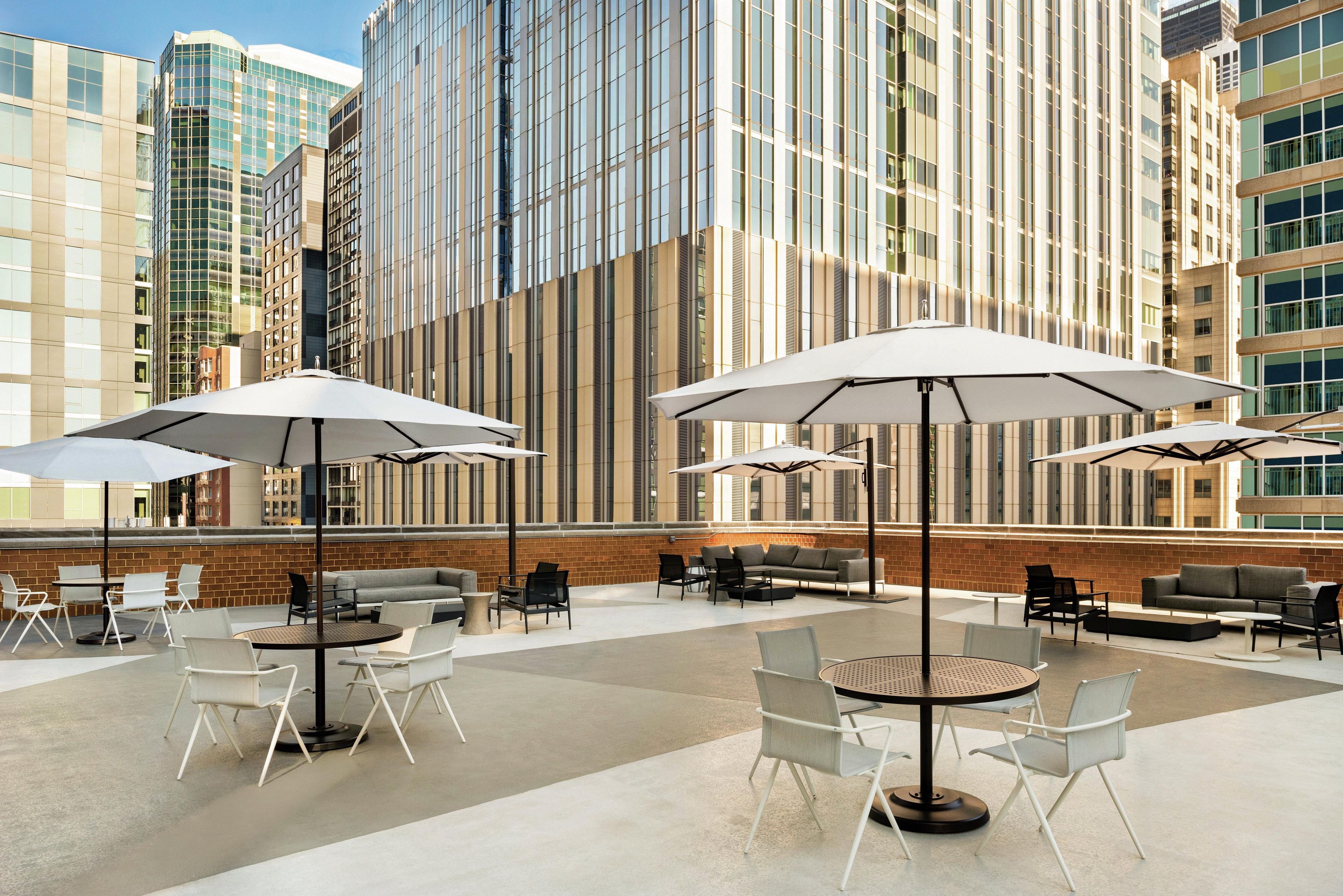 An outdoor seating area with tables and chairs, umbrellas, and a brick wall backdrop.