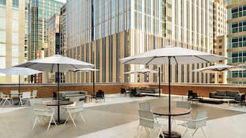 An outdoor seating area with tables and chairs, umbrellas, and a brick wall backdrop.