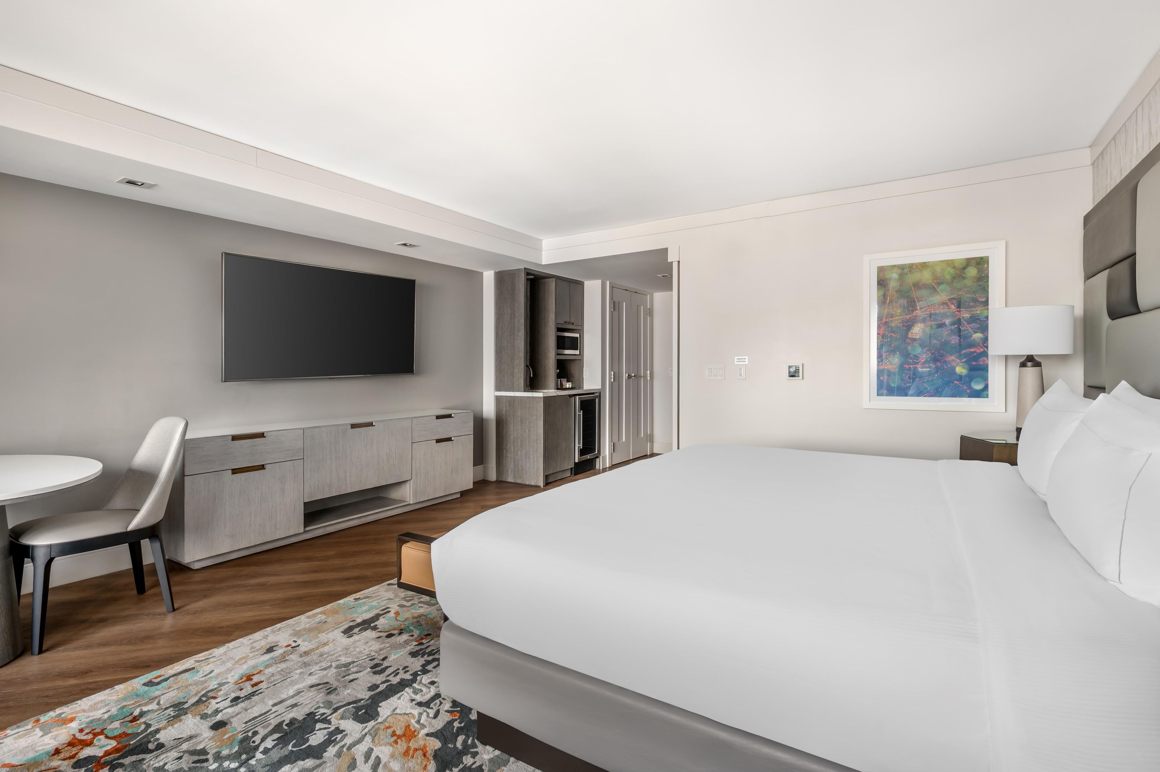 Een moderne hotelkamer met een groot bed, een flatscreen televisie, een bureau met een stoel, een kledingkast en een schilderij aan de muur.
