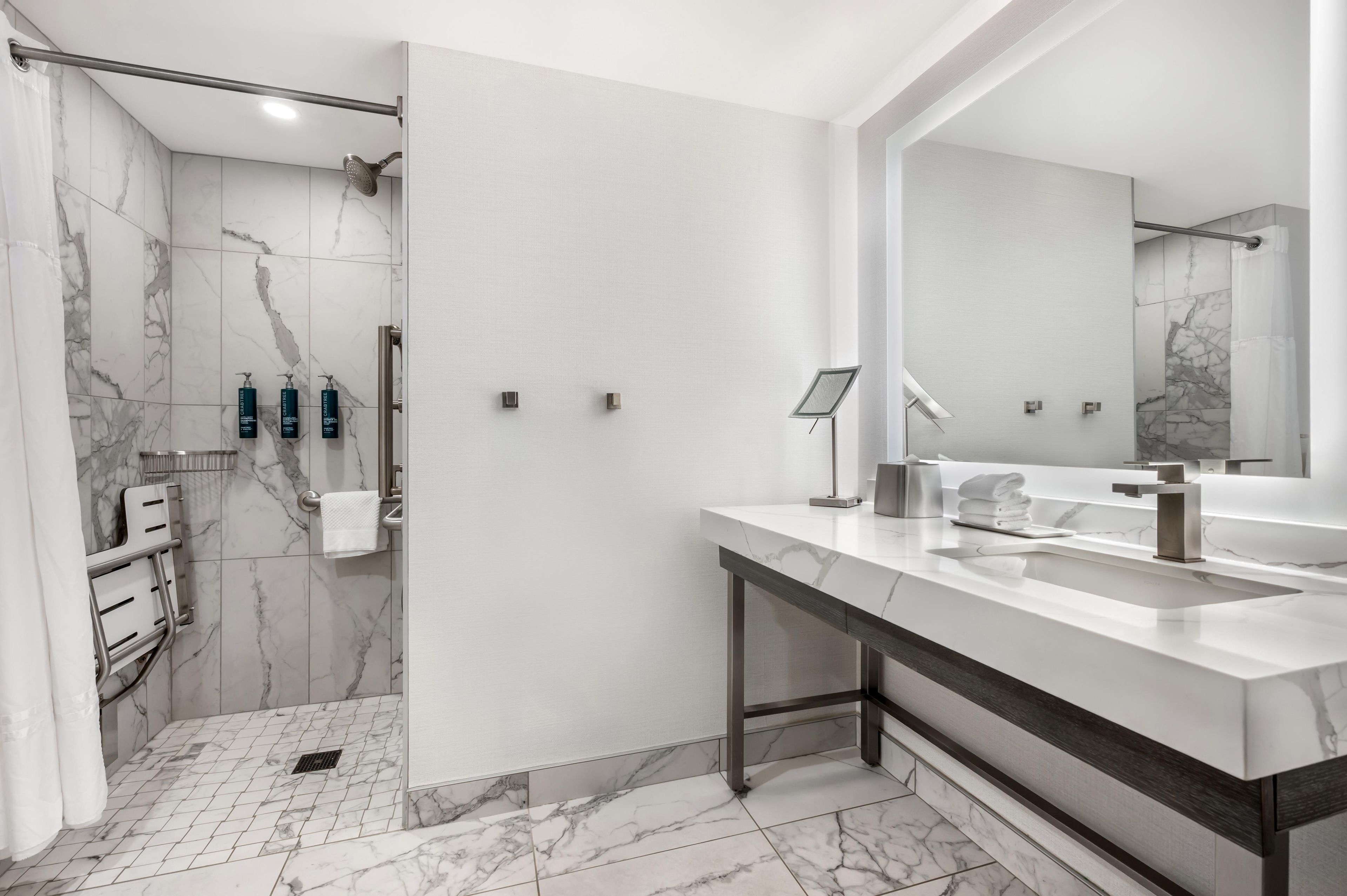 A modern bathroom with a marble floor, a large mirror, a shower, and a vanity with a sink and towel rack.