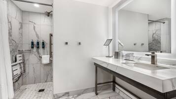 A modern bathroom with a marble floor, a large mirror, a shower, and a vanity with a sink and towel rack.