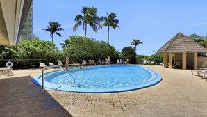 Une piscine dotée de chaises longues et d’un kiosque, entourée de palmiers et d’une terrasse en briques.
