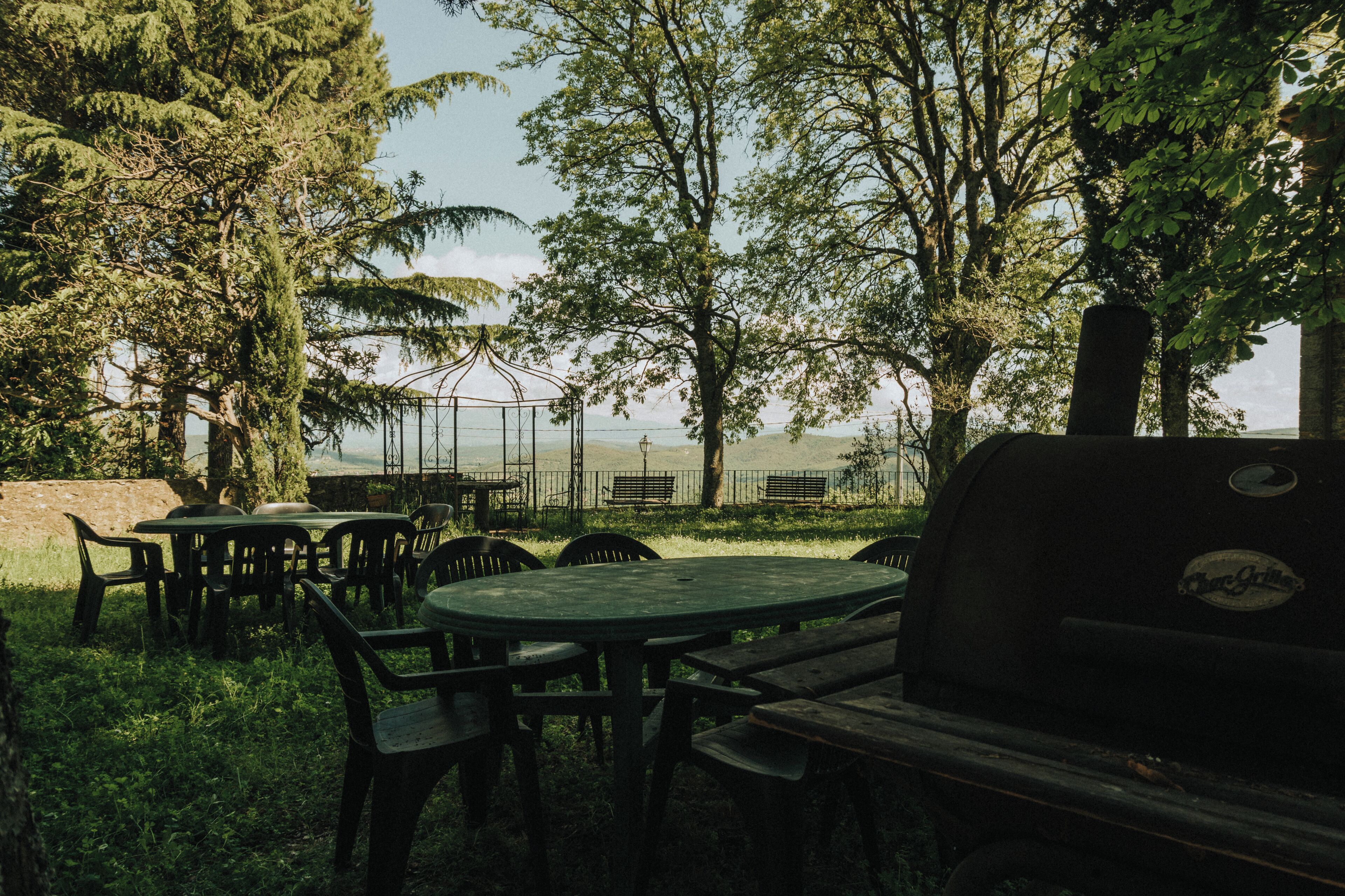 Un'area salotto esterna con tavoli e sedie, circondata da alberi e vista sul mare.