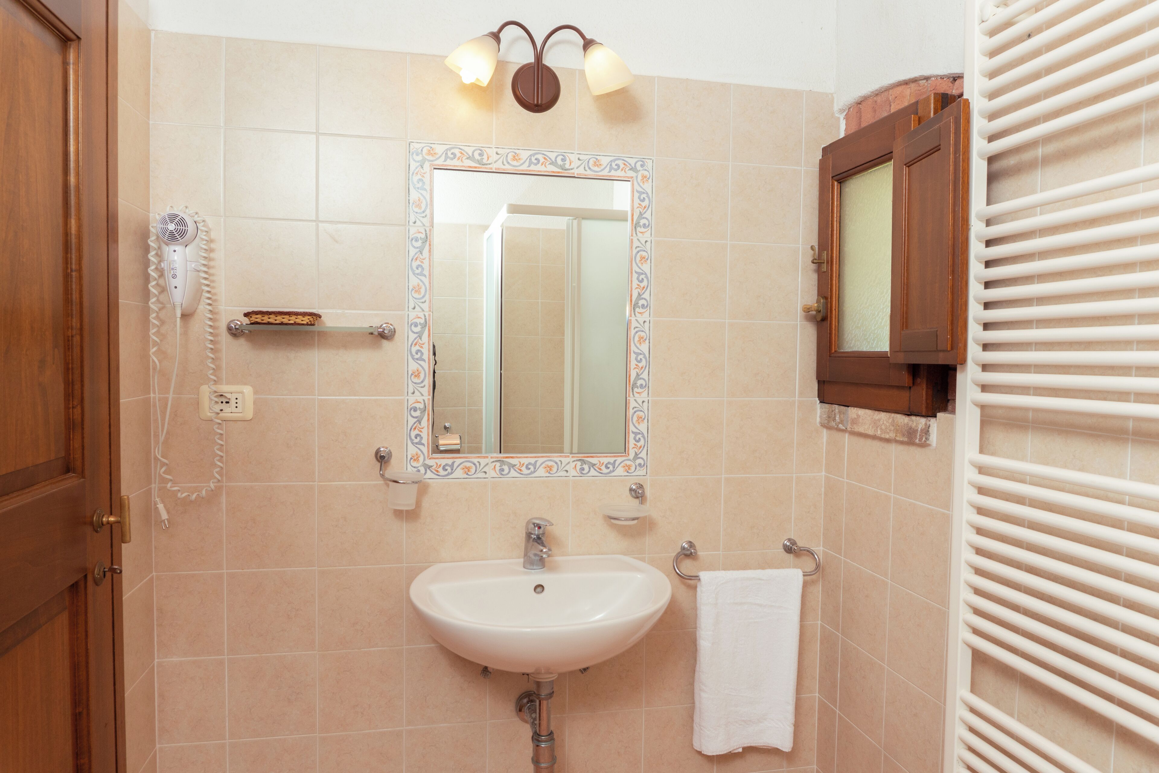 Un baño con lavamanos, espejo, toallero y secador de pelo en la pared.