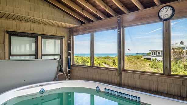 A room with a large window, a wooden ceiling, and a bathtub. - Sea Strapped | Oceanfront + Swim Spa (Topsail Beach)