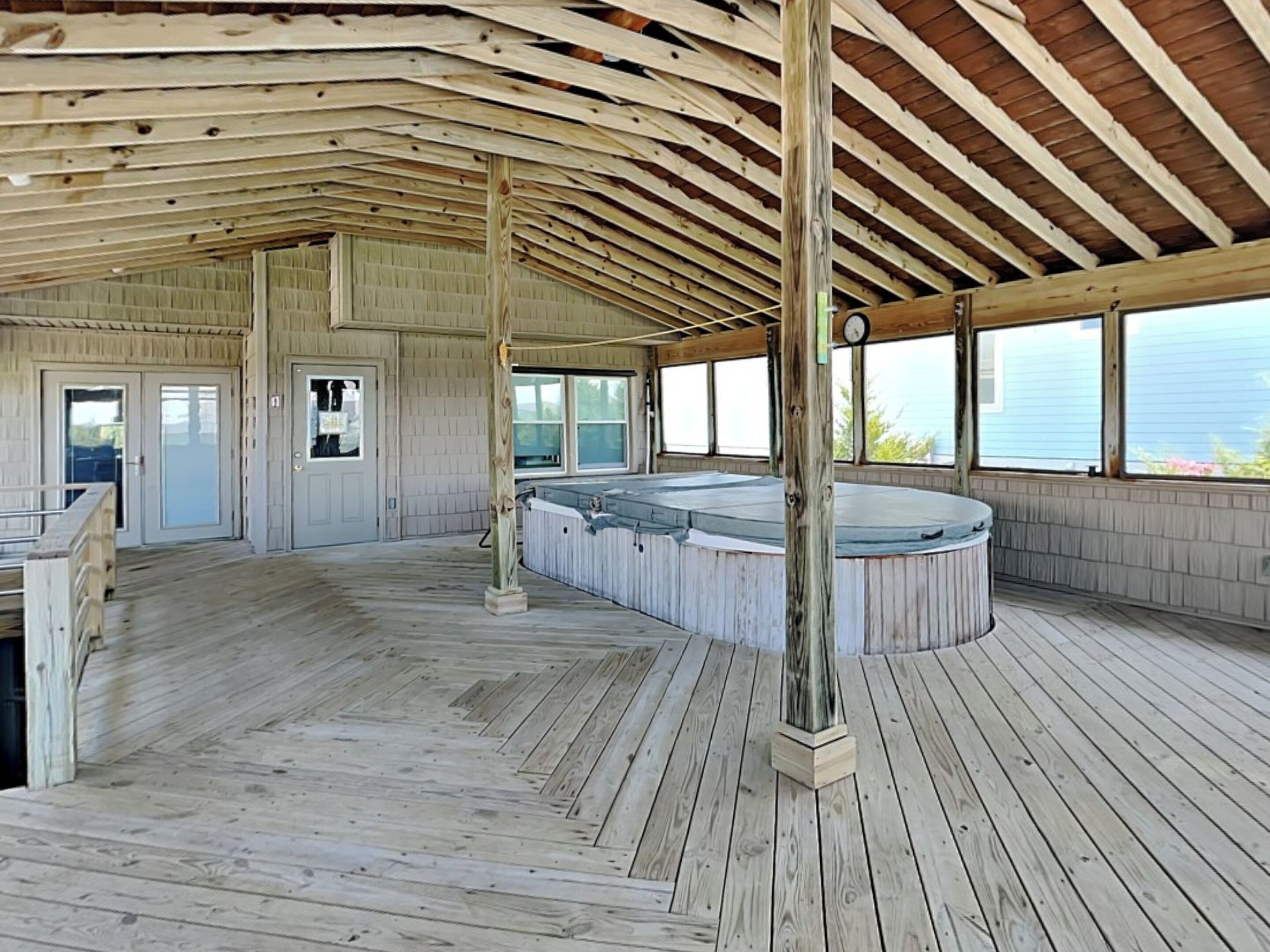An indoor wooden deck with a hot tub, wooden beams, and large windows.