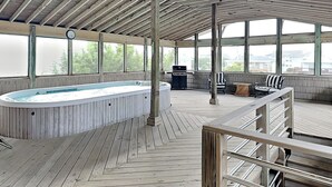 A covered outdoor swimming pool with a wooden deck, a barbecue grill, and a seating area with chairs and a table. - Sea Strapped | Oceanfront + Swim Spa (Topsail Beach)