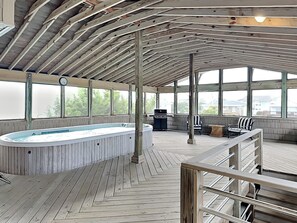 A covered outdoor swimming pool with a wooden deck, a barbecue grill, and a seating area with chairs and a table. - Sea Strapped | Oceanfront + Swim Spa (Topsail Beach)