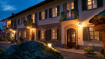 Un edificio a più piani con facciata in pietra, diverse finestre con persiane e un ingresso ben illuminato.