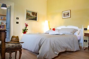 Un dormitorio con una cama, mesitas de noche, una lámpara, un sombrero, una planta en maceta y una estantería.