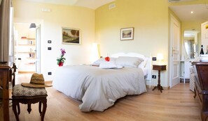 A bedroom with a large bed, bedside tables, a chair, a mirror, and a door leading to another room. - Ca d'I (Magliano Alfieri)