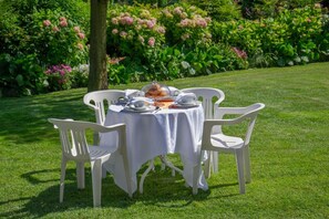 An outdoor dining table with white chairs, surrounded by lush greenery and flowering plants. - Ca d'I (Magliano Alfieri)