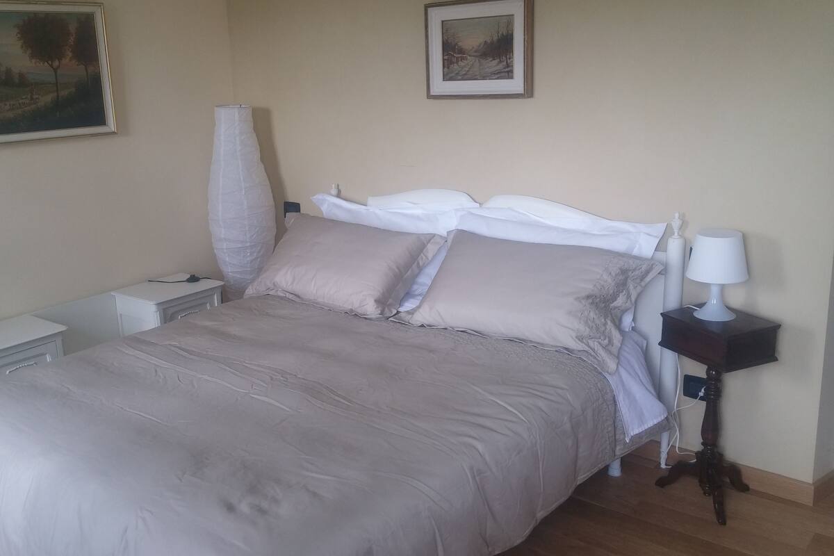 A neatly made bed with a white and beige duvet, a bedside table with a lamp, and two framed pictures on the wall.