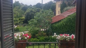 Un balcón con vista a un jardín, un farol y un edificio lejano.