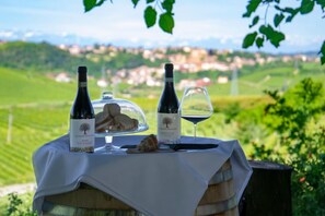 A table set outdoors with two wine bottles, a glass, and a dessert on a wooden barrel. - Ca d'I (Magliano Alfieri)