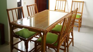 Un espace repas avec une table rectangulaire en bois, entourée de six chaises en bambou dotées de coussins verts.