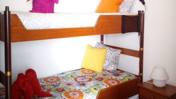 Un lit superposé avec une couverture colorée, des oreillers et un jouet en peluche sur le lit du haut.