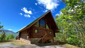 A log cabin with a stone foundation, a wooden deck, and a staircase leading to a porch. - Elkmont Views - 1BR/New Hot Tub/New Firepit/Grill/Sleeps 6 (Gatlinburg)