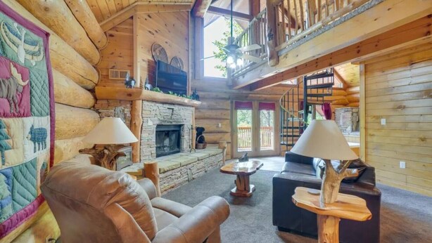A log cabin interior with a stone fireplace, leather sofa, and a quilted wall hanging. - LeConte - 2BR/New Hot Tub/New Firepit/Grill/Sleeps 8 (Gatlinburg)