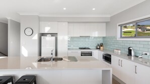 A modern kitchen with white cabinets, a stainless steel sink, and a window overlooking a green landscape. - Time Away - 50 Turnberry Drive (Normanville)