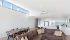 A modern living space with a dining area, a brown sectional sofa, and a kitchen with white cabinets and a tiled backsplash. - Time Away - 50 Turnberry Drive (Normanville)