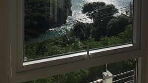 A coastal view through a window, including a cliff, greenery, and the sea. - Famous Marigot Bay Ridge - Safe - Architect 2 bed - Amazing Caribbean views (Marigot Bay)