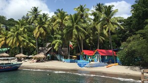 A beach with palm trees, a boat, and a building with a red roof. - Famous Marigot Bay Ridge - Safe - Architect 2 bed - Amazing Caribbean views (Marigot Bay)