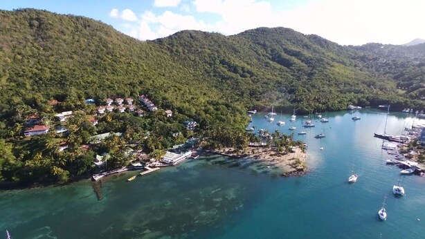 An aerial view of a coastal area with clear turquoise waters, a marina with several boats, and a densely forested hillside. - Famous Marigot Bay Ridge - Safe - Architect 2 bed - Amazing Caribbean views (Marigot Bay)