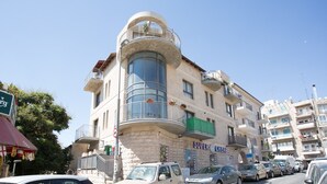 Un immeuble à plusieurs étages doté d’un balcon incurvé, d’une enseigne indiquant « SUPER PRIX » et de plusieurs voitures garées.