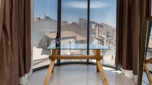 Une pièce avec une fenêtre en verre incurvé, une table en bois sur laquelle se trouvent une bouteille de vin et des verres, et des rideaux marron.