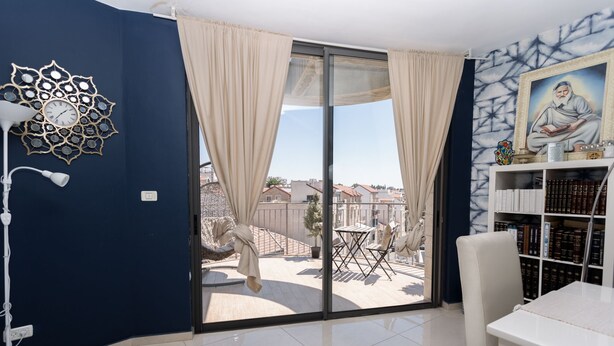 Une pièce dotée d’une grande porte-fenêtre coulissante donnant sur un balcon extérieur, d’un bureau blanc, d’une bibliothèque et d’un élément décoratif mural.
