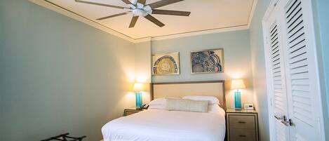 A bedroom with a bed, two bedside lamps, a ceiling fan, and a door with louvered shutters.