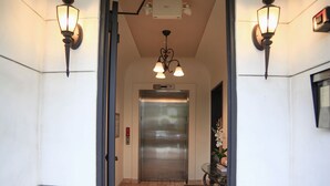 Un pasillo con piso de ladrillo que conduce a un ascensor. Hay luminarias empotradas en la pared a ambos lados de la puerta.