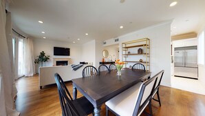 Una cocina moderna con horno integrado, un comedor con mesa y sillas de madera oscura, y un interior blanco.