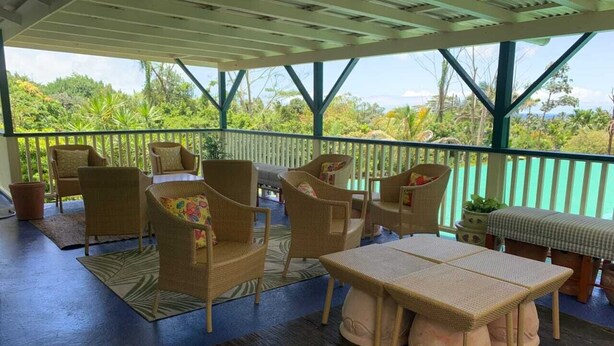 A covered outdoor area with wicker furniture, including chairs and a table, and a view of the surrounding greenery.
