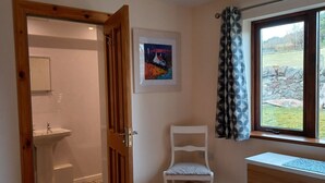 Ein Schlafzimmer mit Bett, Stuhl, Fenster mit Blick, einem Gemälde und einem durch eine geöffnete Tür einsehbaren Badezimmer.